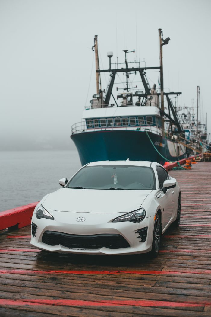 White modern automobile parked on wooden pier near moored big ship on rippling water in coastal area in foggy weather